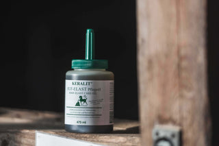 A bottle of Keralit Hufelast care oil stands on a wooden frog in a barn