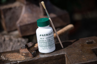 A bottle of Keralit Huffestiger with brush stands on an iron block