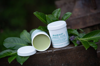 An open and a closed tin of Keralit laurel ointment for horses stand on an iron table with leaves.