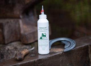 A bottle of Keralit Strahl Liquide stands on an iron bench together with horseshoes and forging tools