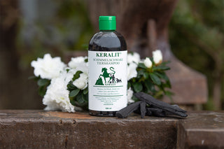 A bottle of horse shampoo Keralit Schimmelschwarz stands on an iron block with flowers in the background.